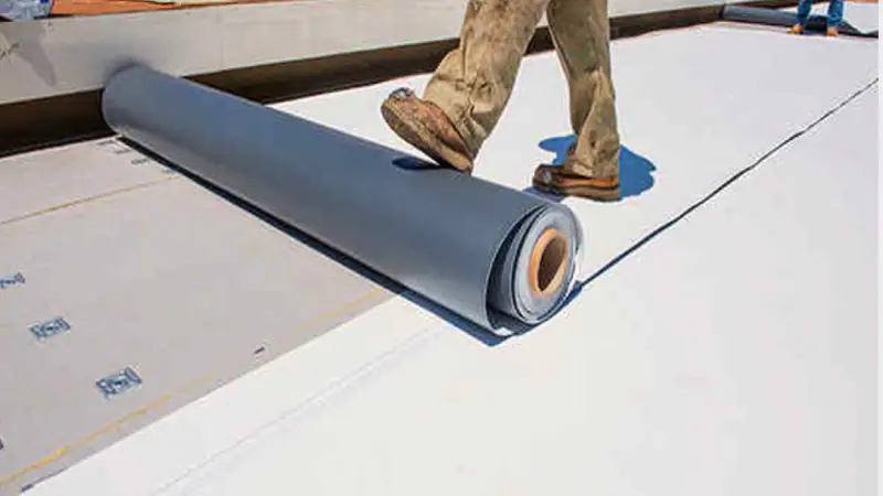 Roofer rolling out white TPO membrane on a low-slope commercial roof